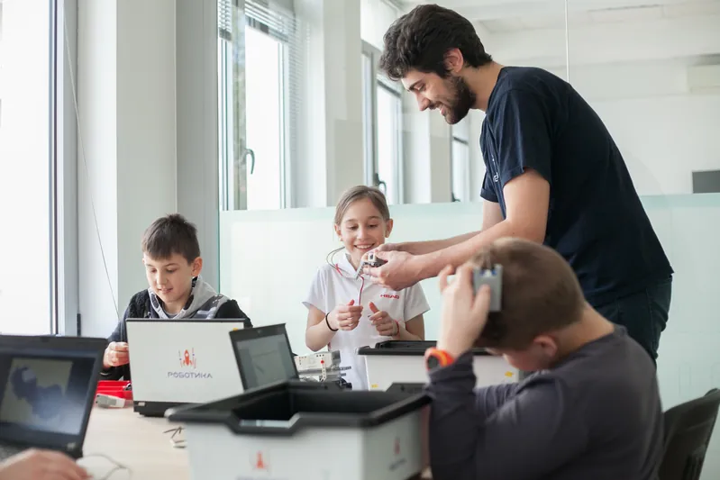 Преподавател помага на деца с роботите в Академия Роботика